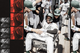 A joyful baseball player in a helmet and uniform sits in a laundry cart while teammates push and cheer around him in a dugout walkway.